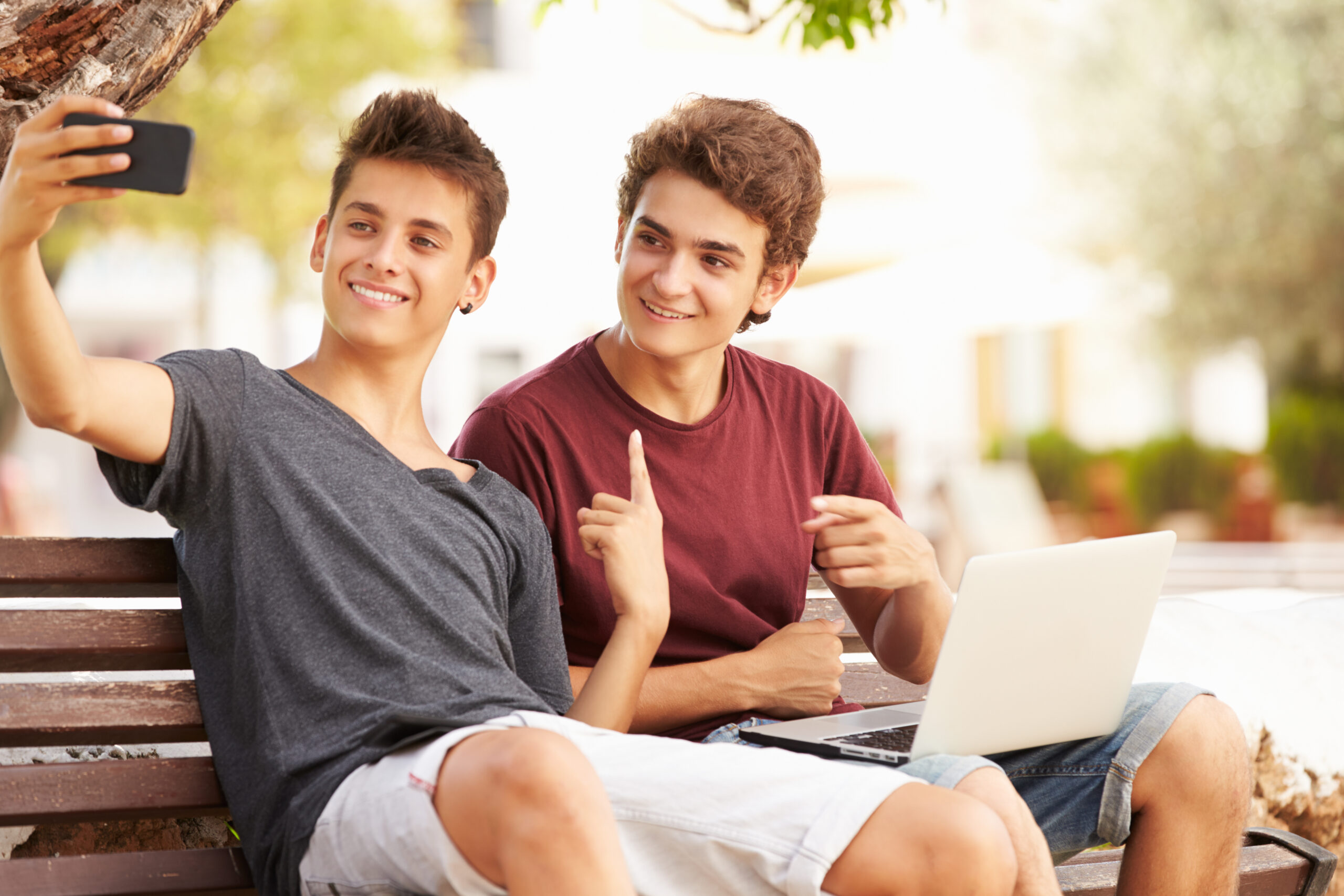 Two,Teenage,Boys,Sitting,On,Bench,Taking,Selfie,In,Park